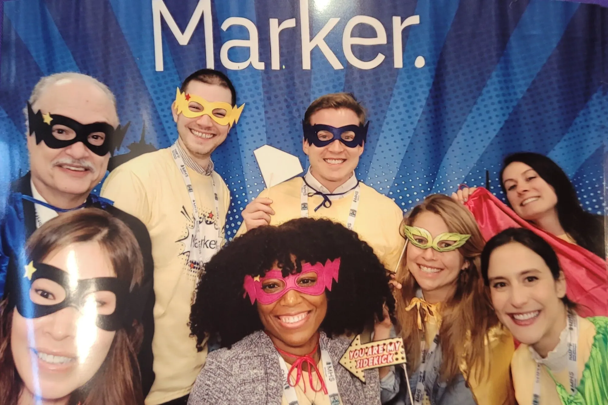 Dr. Ortiz and seven Marker teammates wearing superhero masks in front of a Marker backdrop.